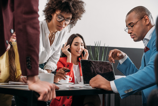 A group of professional women and a man gather at an office table to collaborate.