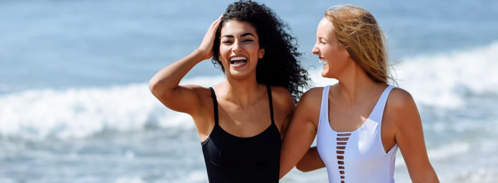 happy female couple walking down the beach in swimsuits