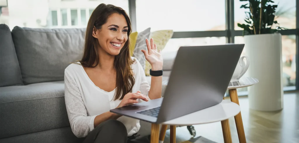 cheerful woman on laptop video call waving to the camera